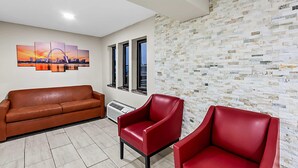 Una habitación con un sofá de cuero marrón, una silla roja y un cuadro de un paisaje urbano en la pared.