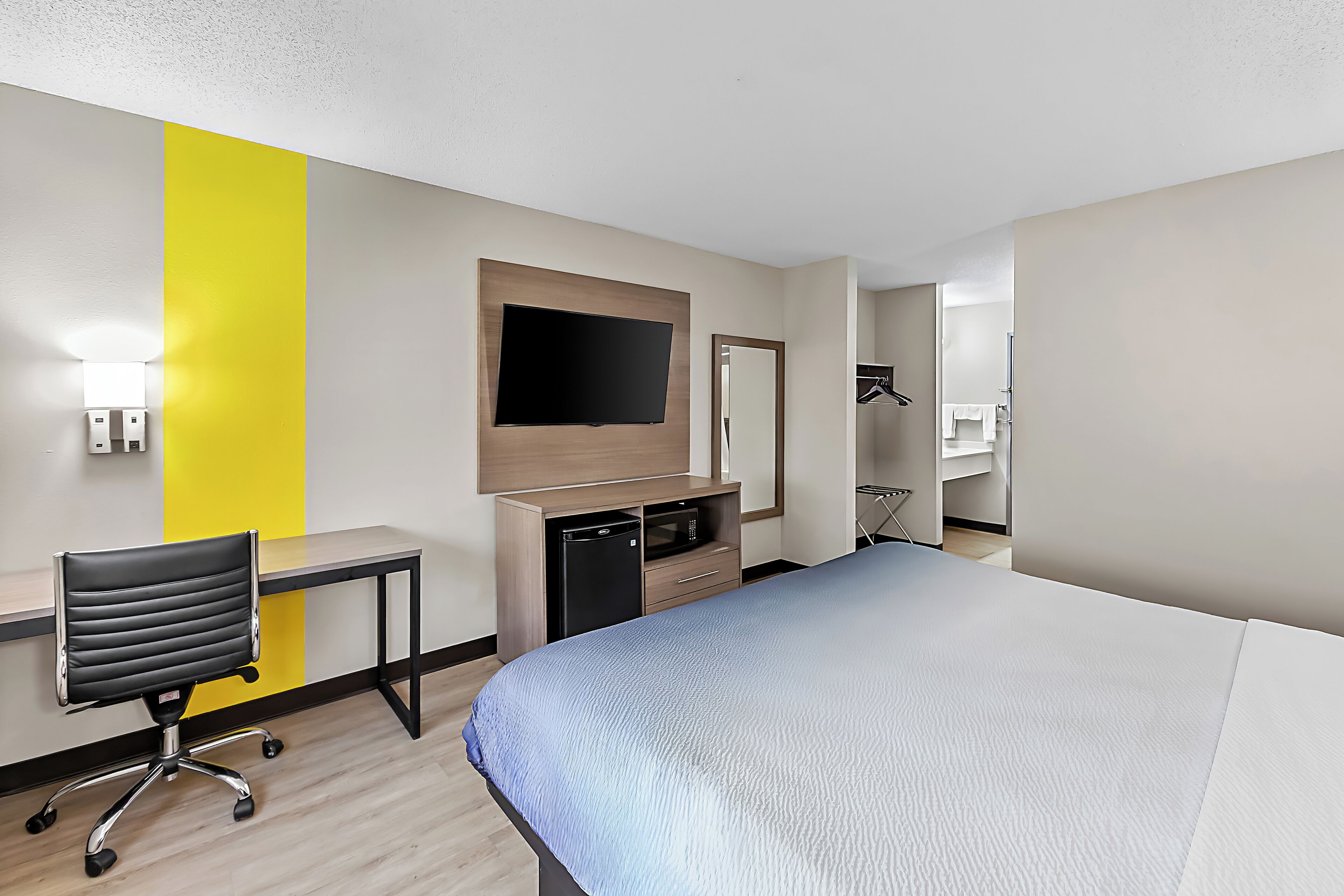 A hotel room with a bed, desk, chair, TV, microwave, and a mirror.