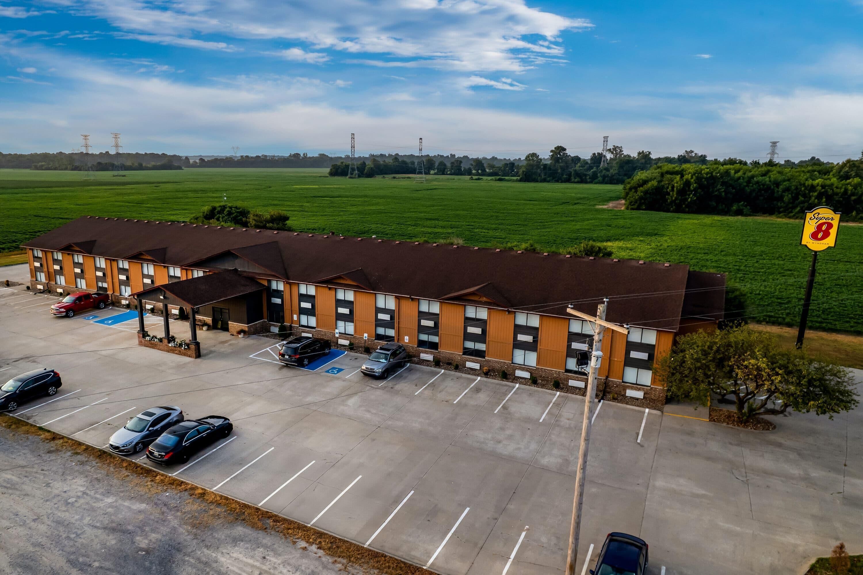 A hotel with a parking lot, a sign indicating the number of rooms, and a view of a green field.