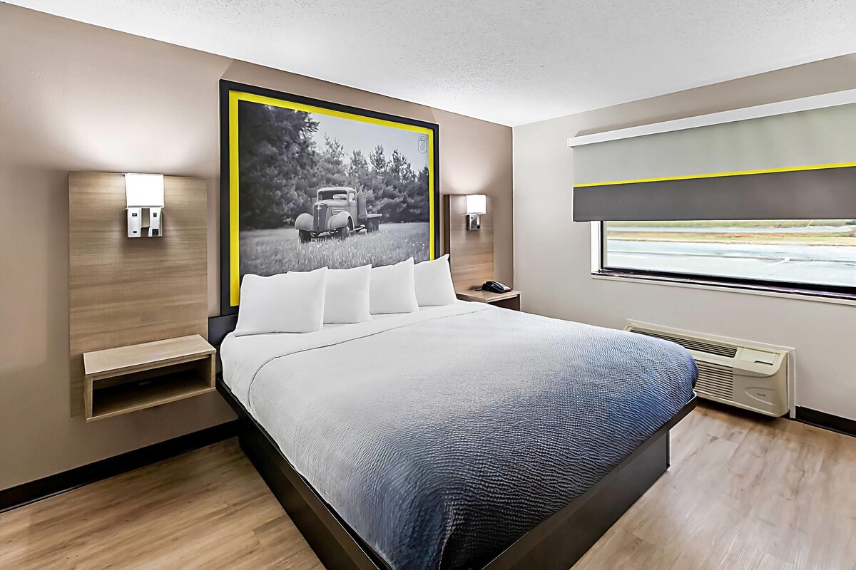 A modern hotel room with a large bed, bedside tables, a wall-mounted air conditioning unit, and a window with a view.