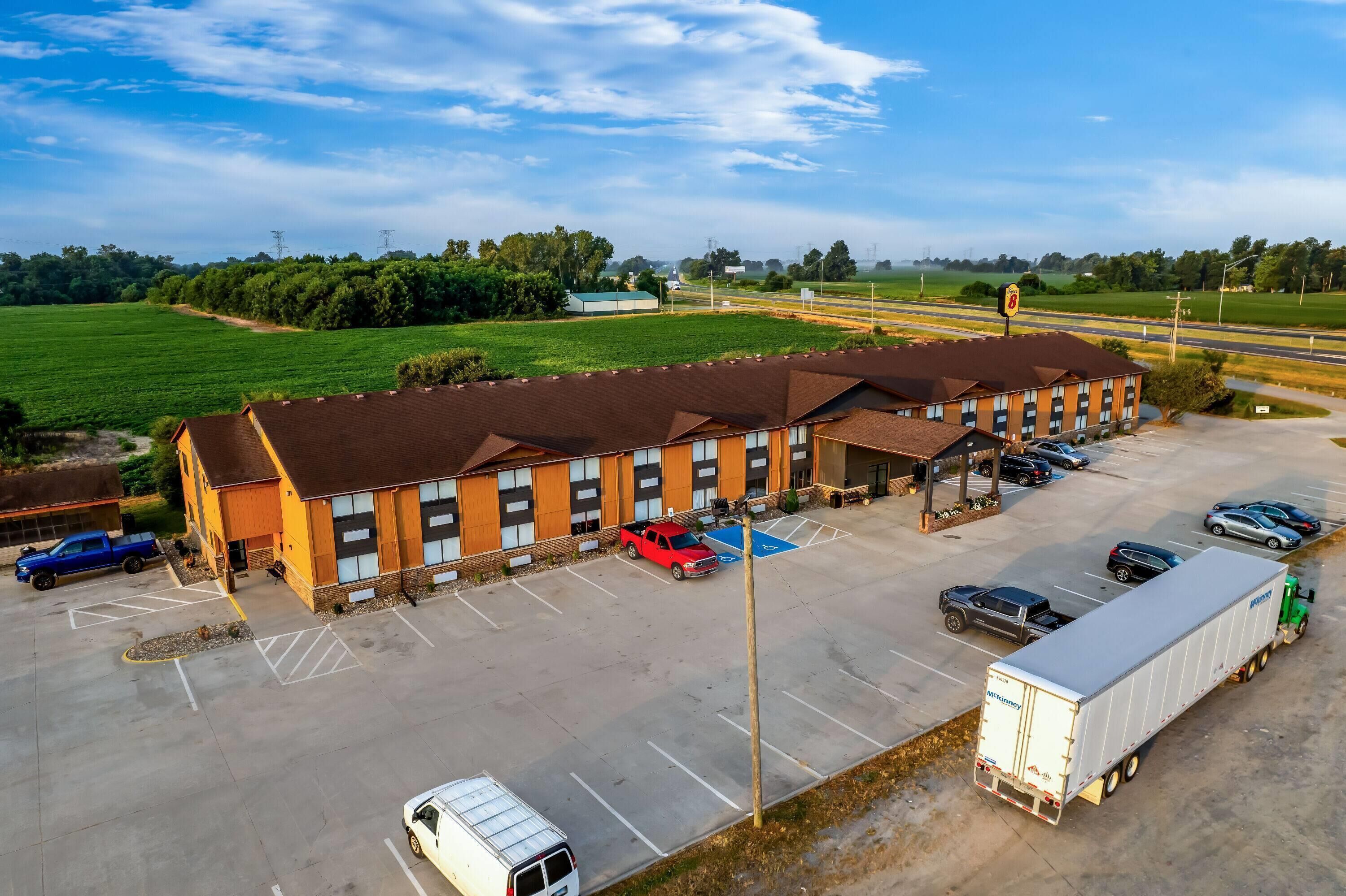 A large parking lot with multiple vehicles, including a white van, a blue truck, and a red pickup truck. There is a large building with a brown roof and multiple windows.
