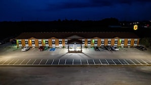 Un hotel con entrada central, varios espacios de estacionamiento y fachada bien iluminada.