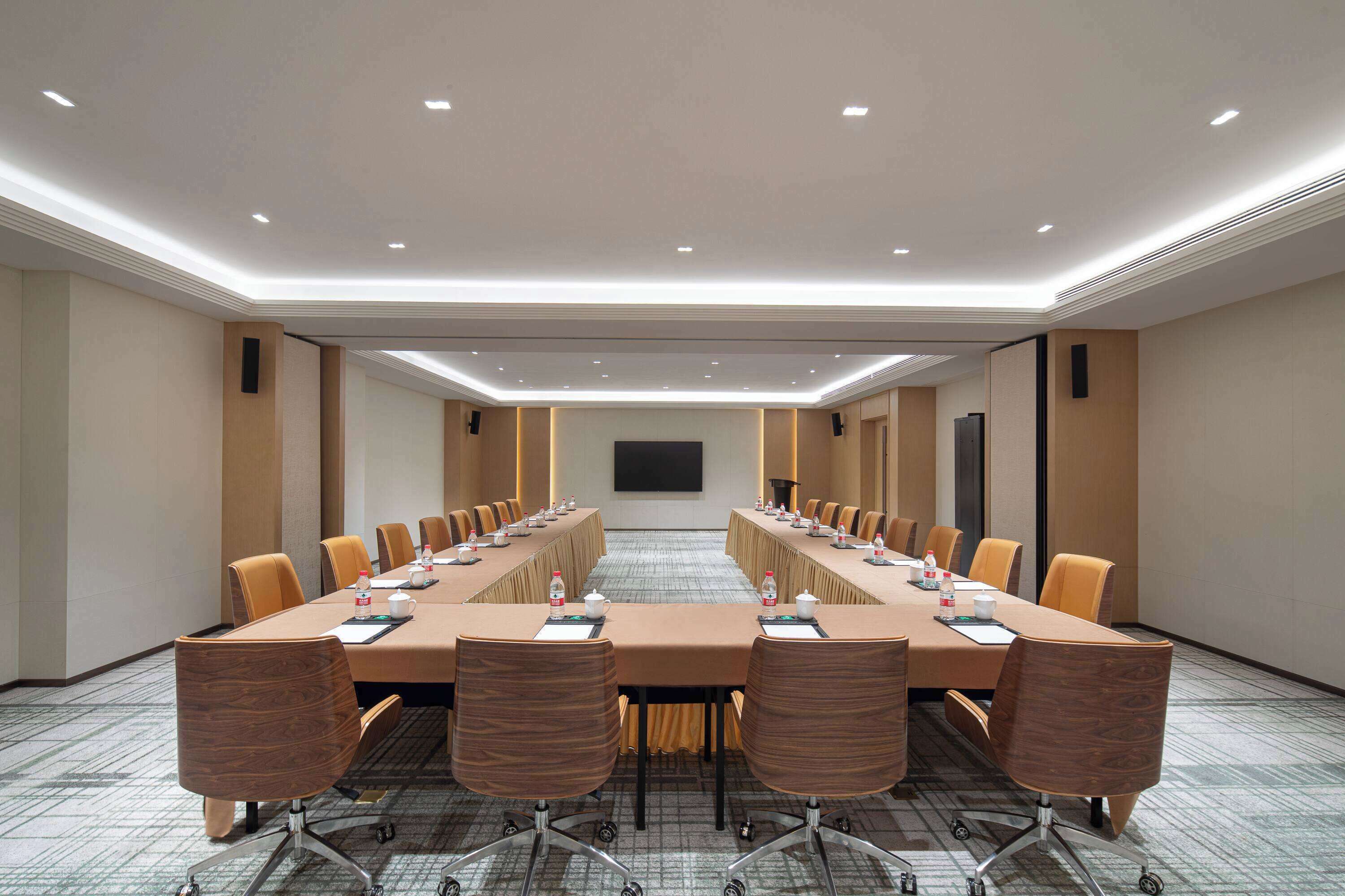 Un salón de conferencias con una larga mesa, sillas y una pantalla de proyector.