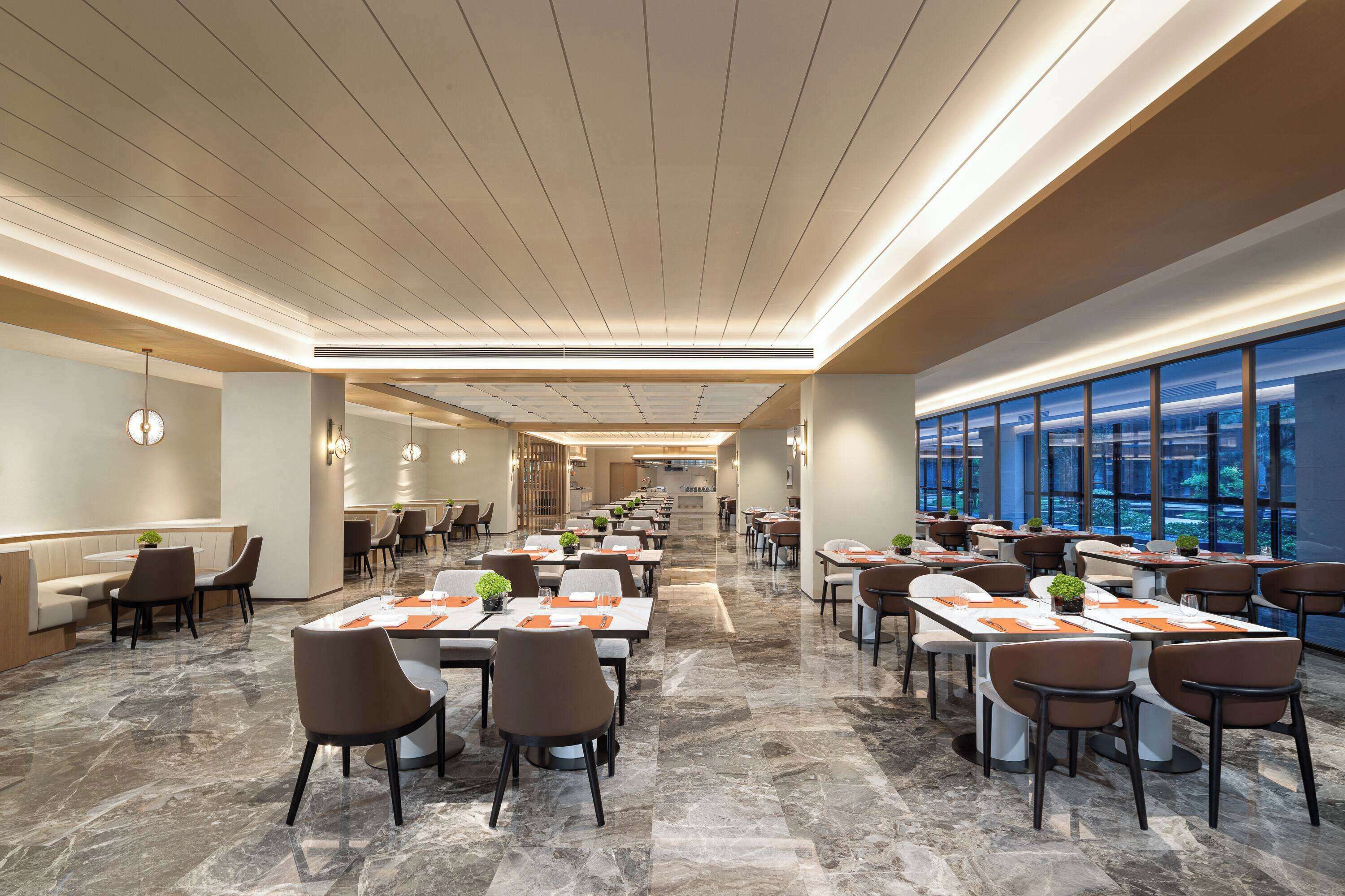 A spacious dining area with marble flooring, modern lighting, and large windows offering views of the city.