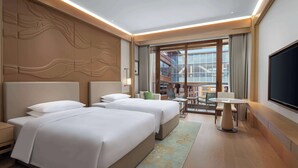 Ein Hotelzimmer mit zwei Betten, einem Schreibtisch, einem Stuhl, einem Fernseher und einem Balkon mit Stadtblick.
