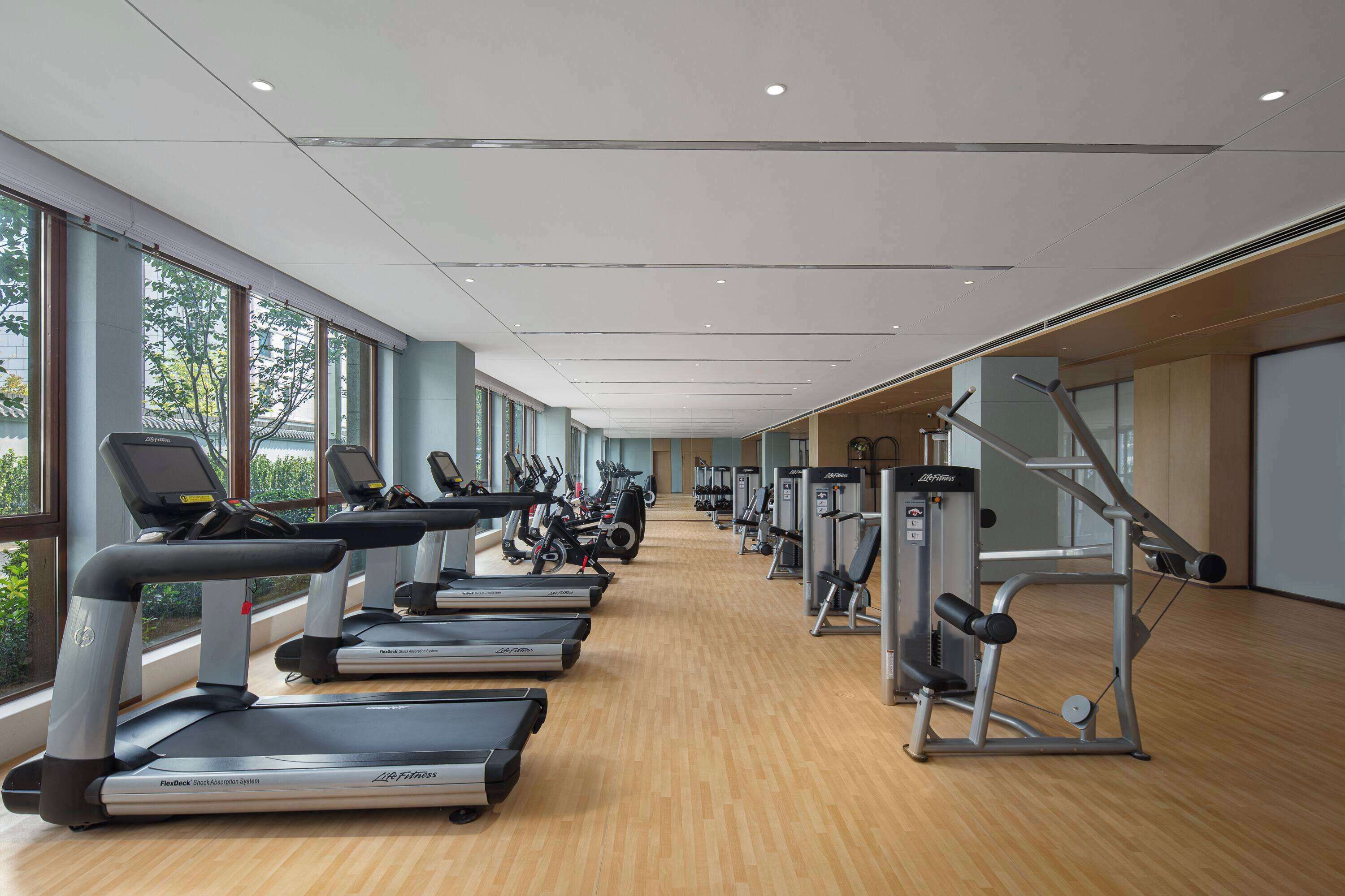 A gym with treadmills, ellipticals, and weight machines arranged in a spacious, well-lit room with large windows.