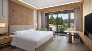 Ein modernes Hotelzimmer mit einem großen Bett, einem Flachbildfernseher, einem Balkon mit Tisch und Stühlen sowie einem schönen Ausblick.