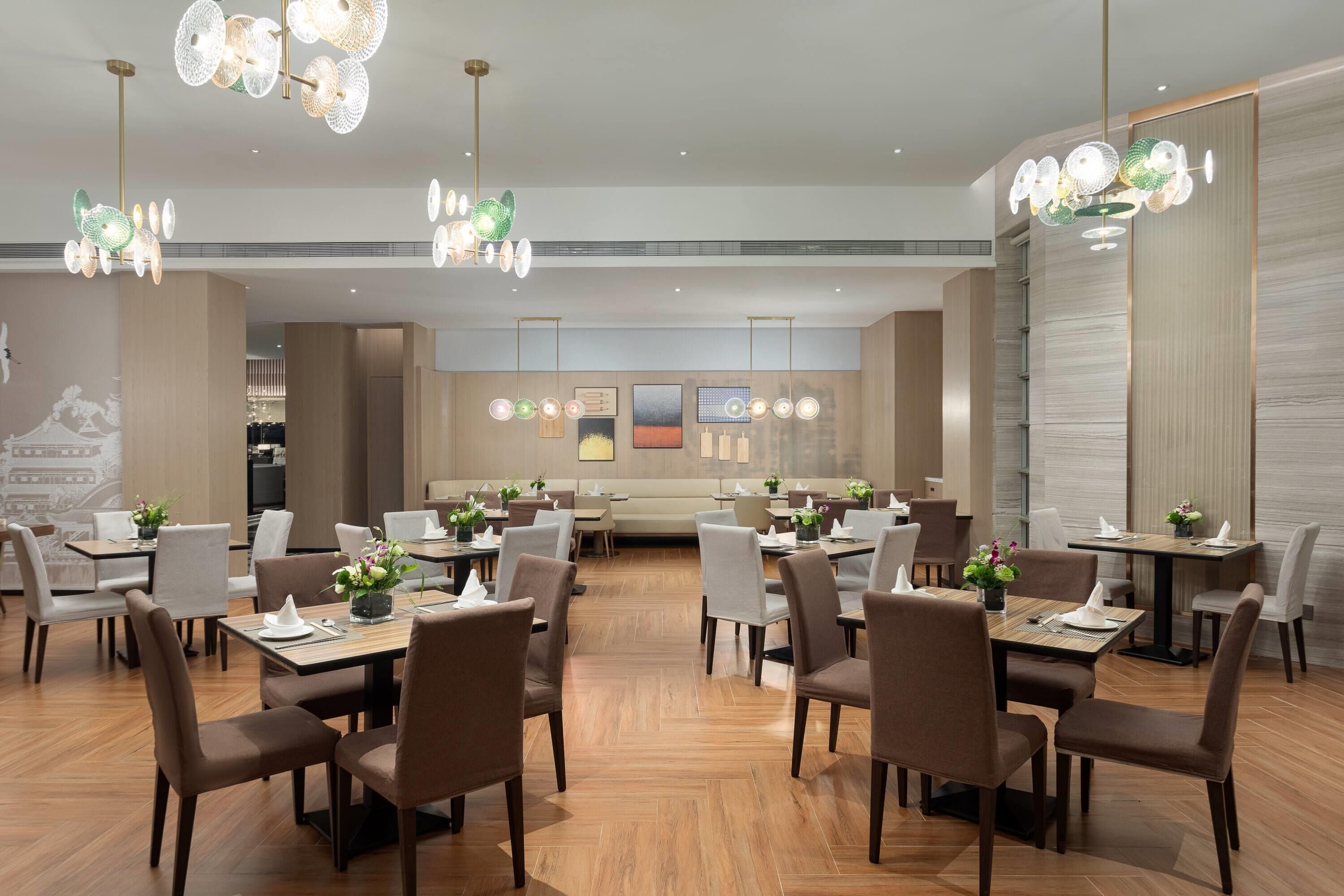 A modern restaurant with wooden flooring, brown chairs, and tables set for dining.