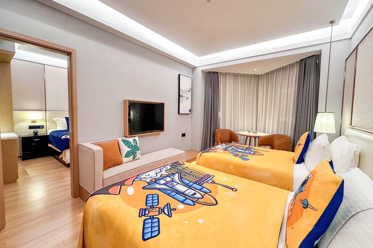 A hotel room with two beds, a sofa, a TV, a desk, and a window with curtains.