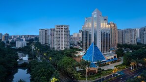 A modern cityscape with high-rise buildings, a prominent blue glass structure, and a river with greenery. - Wyndham Garden Haikou Meilan (Haikou)