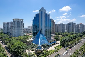 A modern high-rise building with a distinctive pyramid-shaped structure, surrounded by palm trees and other high-rise buildings. - Wyndham Garden Haikou Meilan (Haikou)
