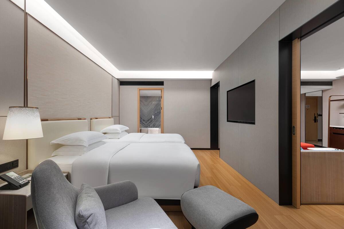 A modern hotel room with a bed, bedside tables, a desk, and a chair.