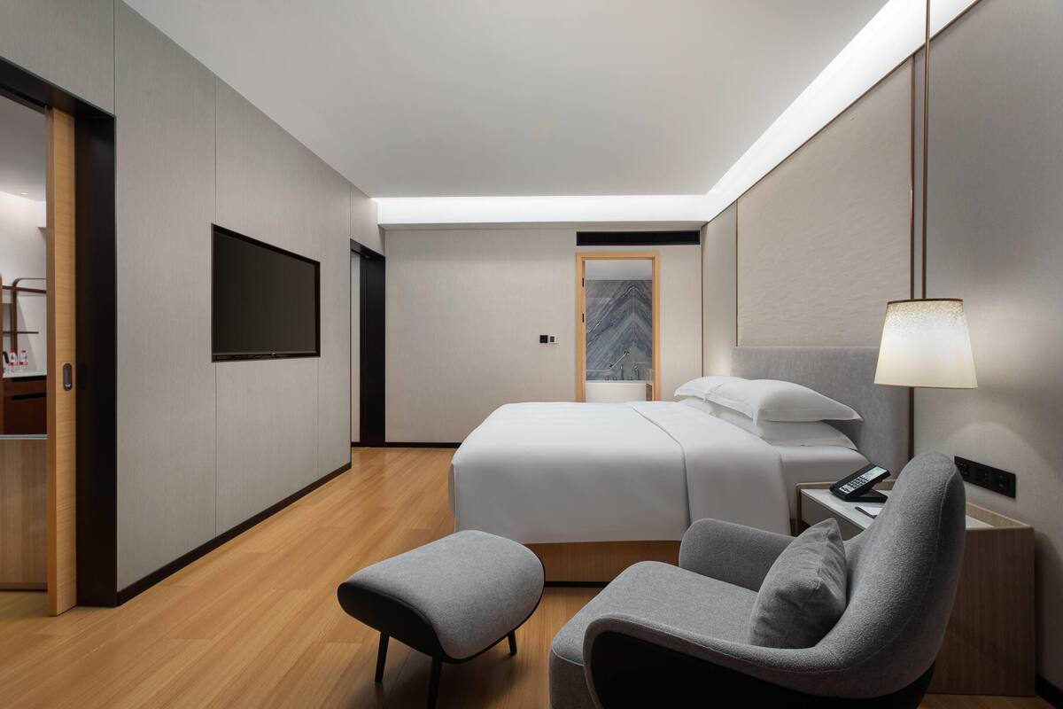 A modern hotel room with a bed, a desk, a chair, and a TV.