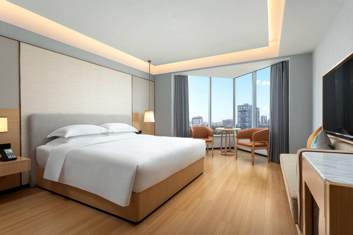 A modern hotel room with a large bed, a desk, a chair, and a TV.