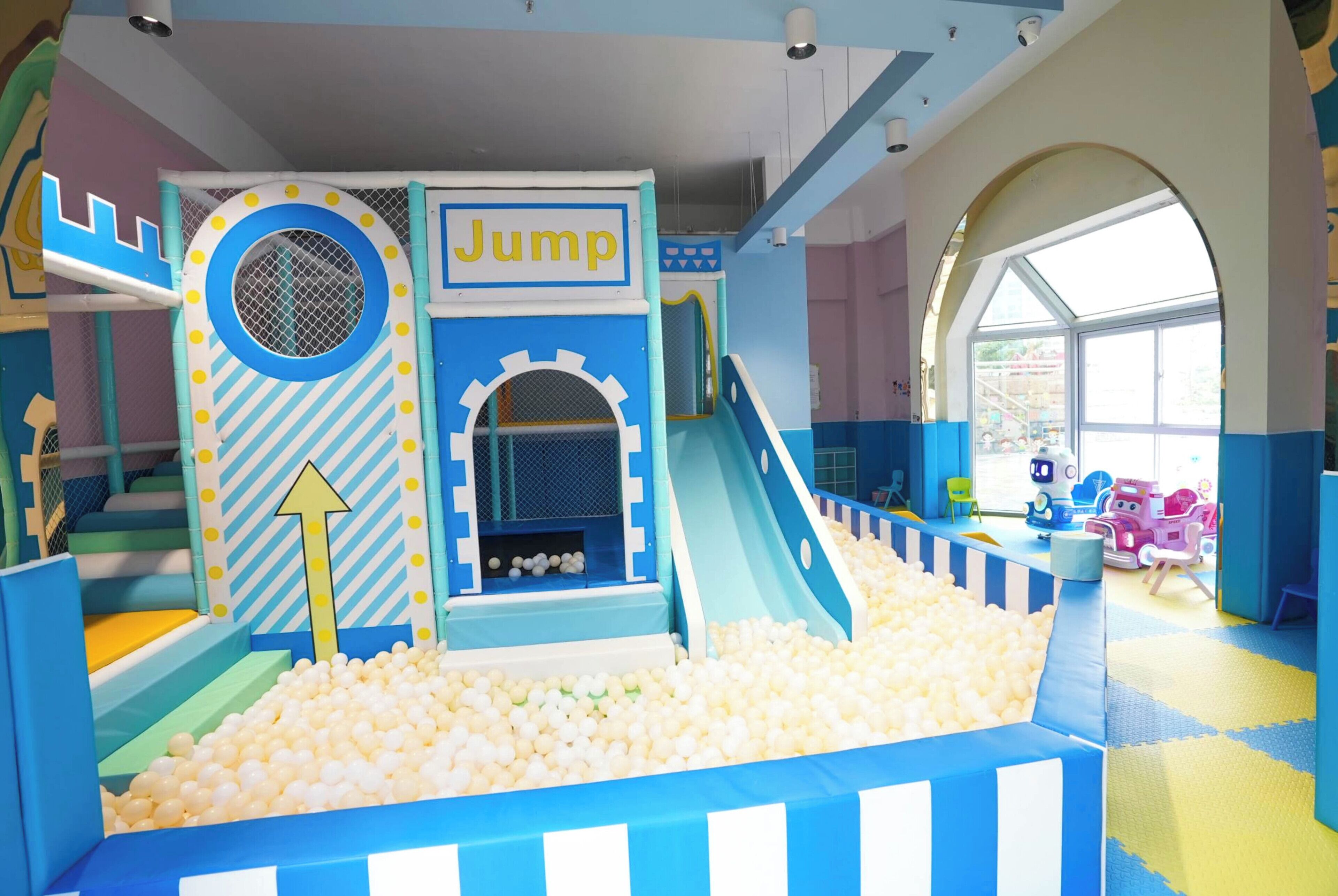 Uma área de recreação infantil com piscina de bolinhas, escorregador e estrutura para saltar.