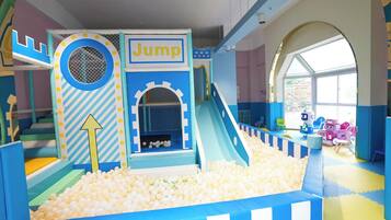 Uma área de recreação infantil com piscina de bolinhas, escorregador e estrutura para saltar.