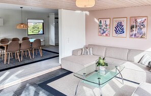 En moderne stue med et glasbord, en beige sofa og et spiseområde med stole og bord.