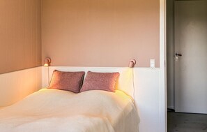 En seng med to puder, en lampe på væggen og en dør.