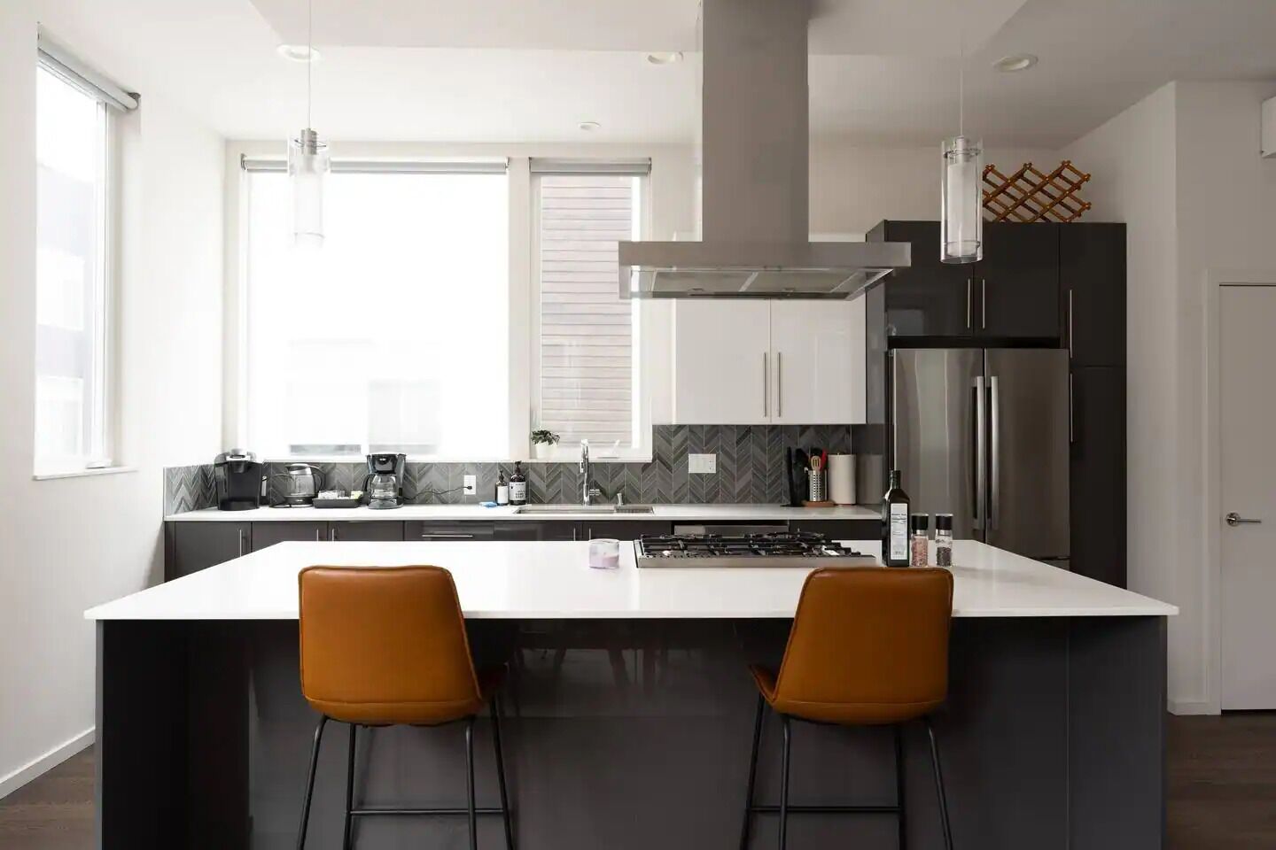 A modern kitchen with a central island, two bar stools, a refrigerator, and a coffee maker.