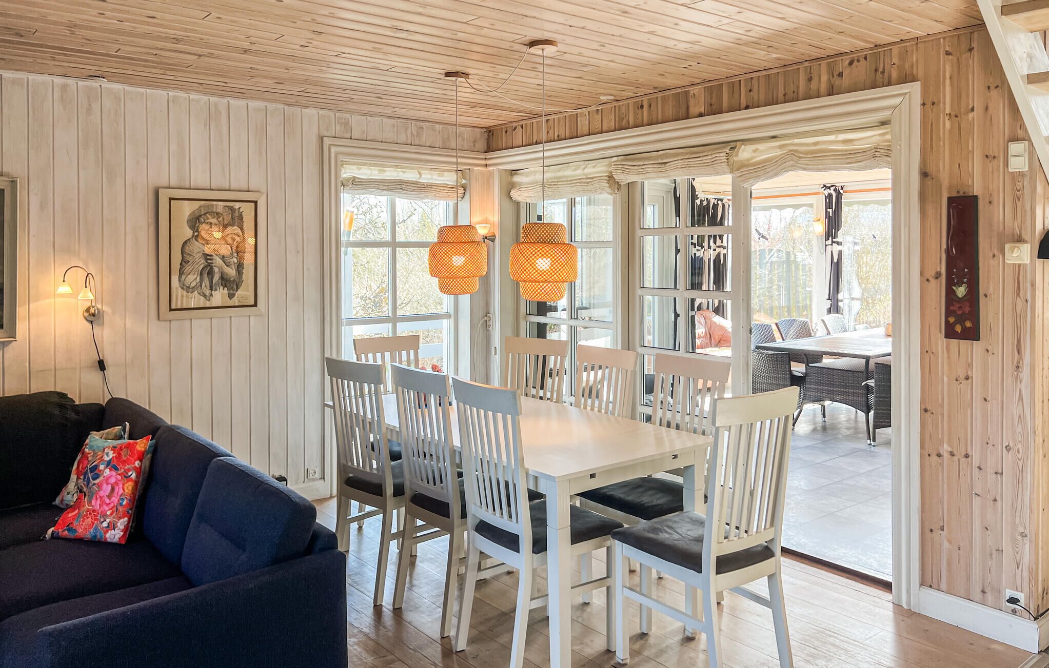 Et spiseområde med et hvidt bord og stole, en sofa med farverige puder, og et træloft.