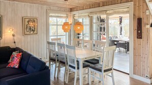 Un coin repas avec une table et des chaises blanches, un canapé agrémenté de coussins colorés et un plafond en bois.