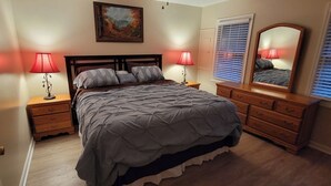 A bedroom with a bed, two bedside tables, a dresser, a mirror, and a painting on the wall.