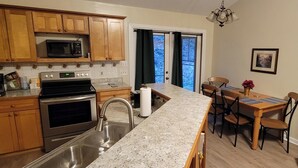 A kitchen with wooden cabinets, a granite countertop, stainless steel appliances, and a dining area with a stone fireplace.