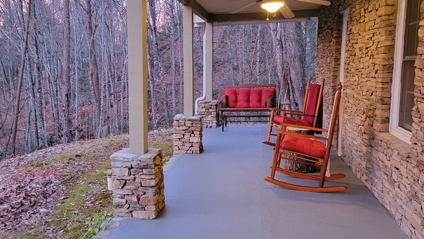 A covered porch with a stone wall, a red rocking chair, and a stone bench.