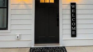 A house with a black front door, a 'WELCOME' sign, and two wall-mounted lights. - Glamorous Hideaway (Gainesville)