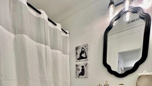 A bathroom with a white toilet, a white sink with a mirror, and a shower curtain. There are two wall-mounted lights above the mirror. - Glamorous Hideaway (Gainesville)