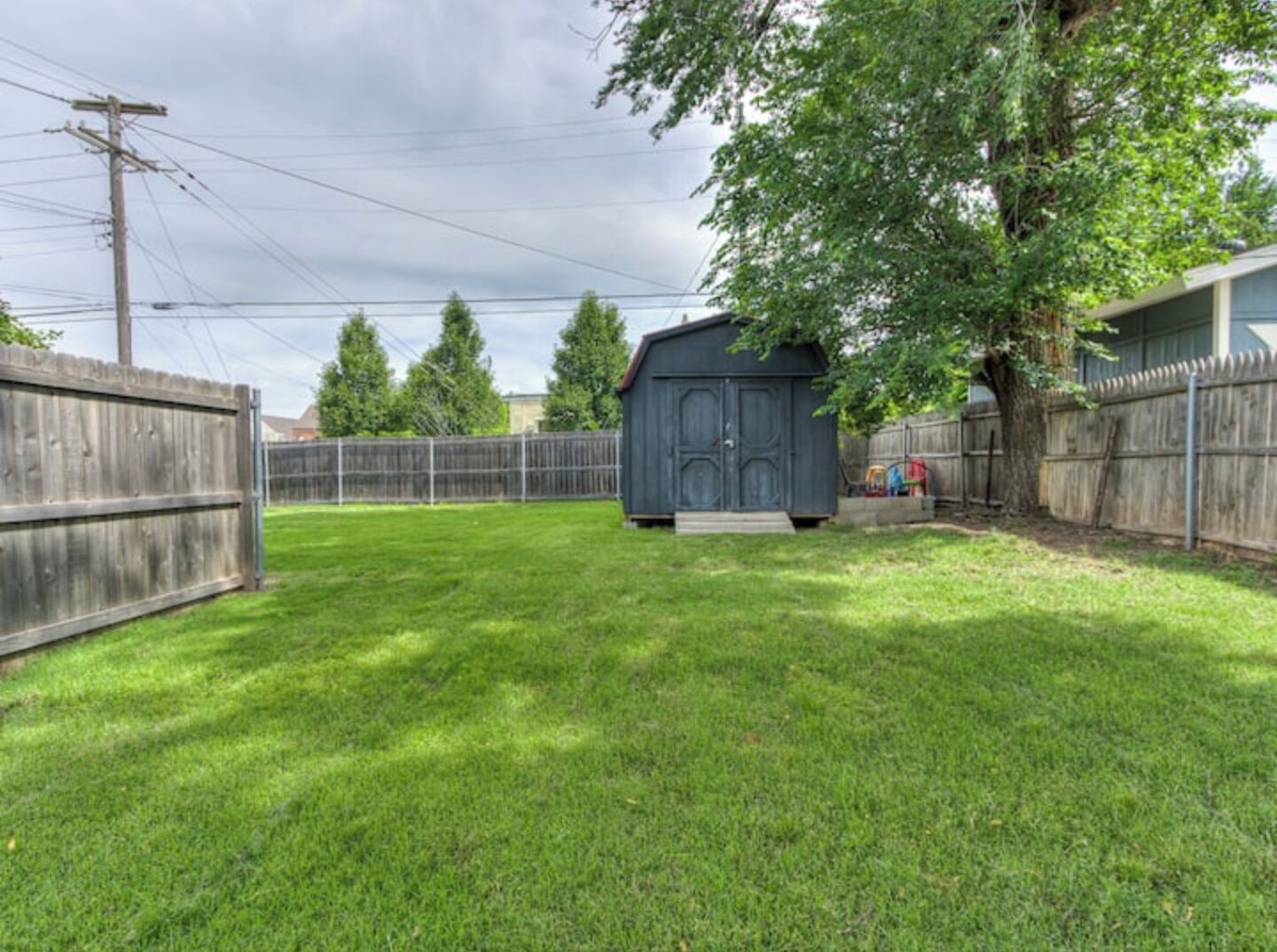A backyard with a shed, a wooden fence, and a tree.
