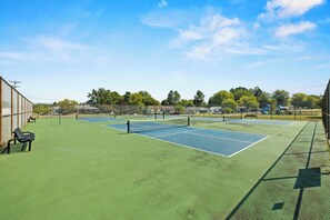 Un court de tennis en plein air, équipé d’un filet, de bancs et d’une clôture.