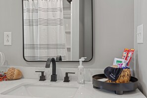 Une salle de bain avec un lavabo blanc, un robinet noir et un miroir au-dessus. On y trouve un porte-serviettes avec une serviette, un distributeur de savon et un petit bol sur lequel est posée une autre serviette.