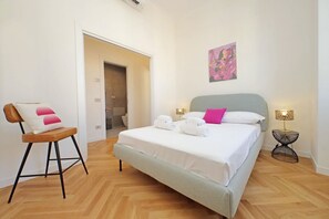 A hotel room with a bed, a chair, a painting, and a lamp.
