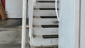 Uma escadaria com degraus brancos que leva a uma porta, uma geladeira branca e uma janela com vista para árvores.