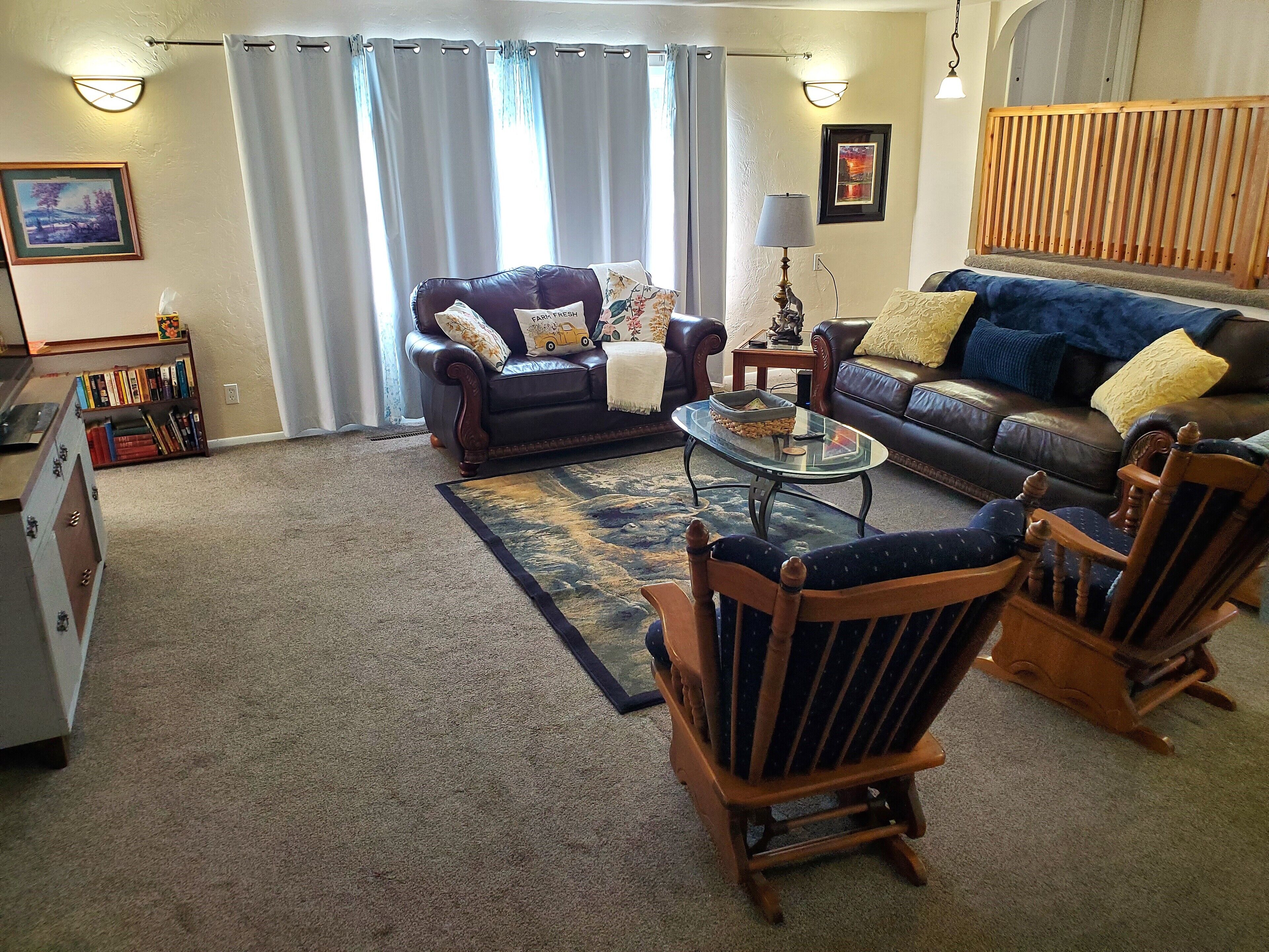 A living room with a leather sofa, two wooden chairs, a glass coffee table, and a bookshelf.