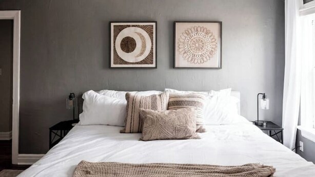 A neatly made bed with white linens and several pillows, a woven throw blanket, and two framed wall art pieces above the bed. - 7 min to Downtown / W/D / Historic / Central (Oklahoma City)