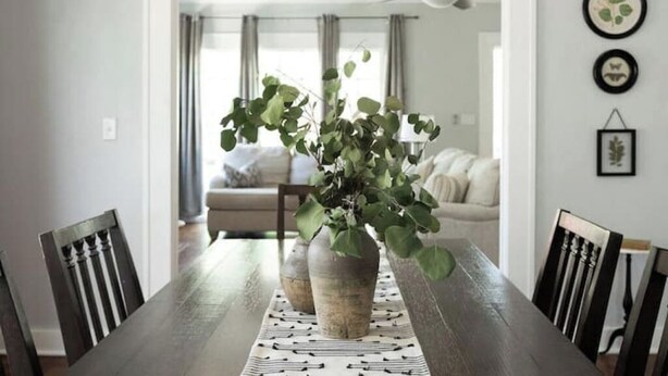 Un coin repas avec une table en bois, deux vases contenant des plantes vertes et un chemin de table à motifs.