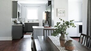 Une cuisine moderne avec des meubles gris, un îlot central et un coin repas comprenant une table et des chaises en bois.