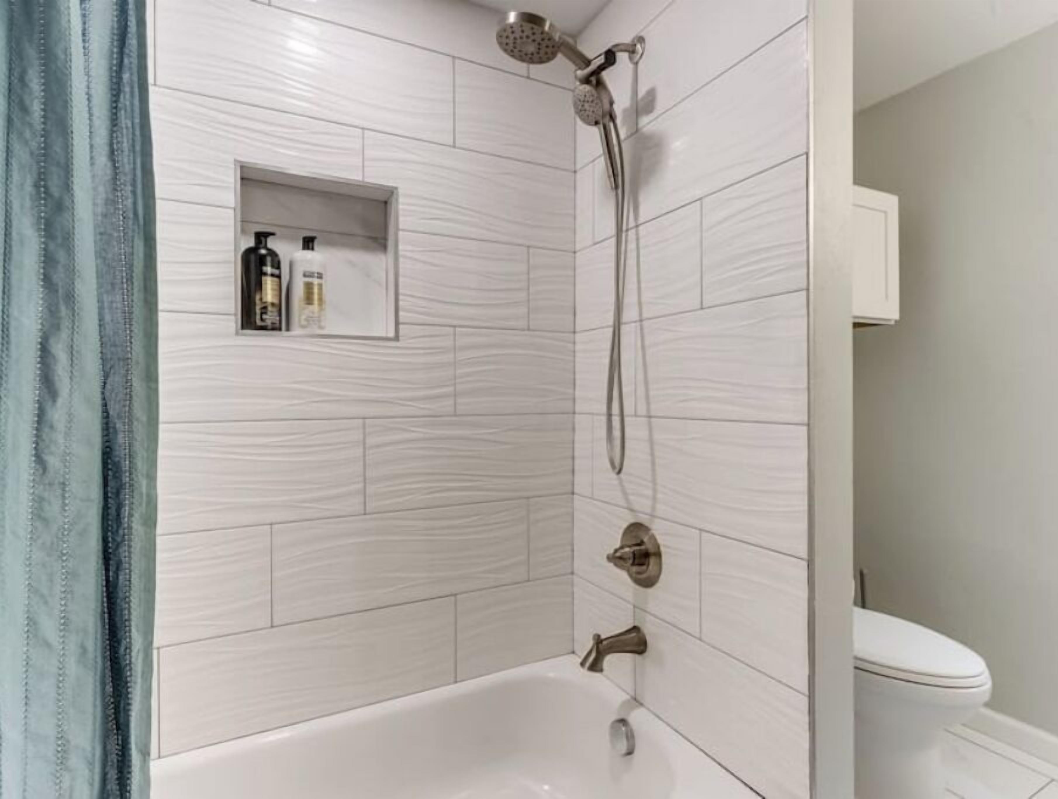 A bathroom with a bathtub, shower, and toilet. There is a shelf with toiletries.