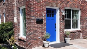 A red brick building with a blue door, a window with a white frame, and a small potted plant on the sidewalk. - Perfect for Large Groups /Walkable /Plaza (Oklahoma City)
