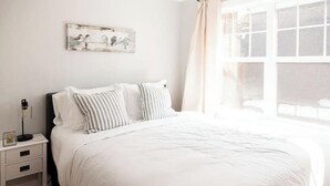 A bedroom with a large bed, white bedding, a nightstand with a lamp, and a window with curtains. - Perfect for Large Groups /Walkable /Plaza (Oklahoma City)