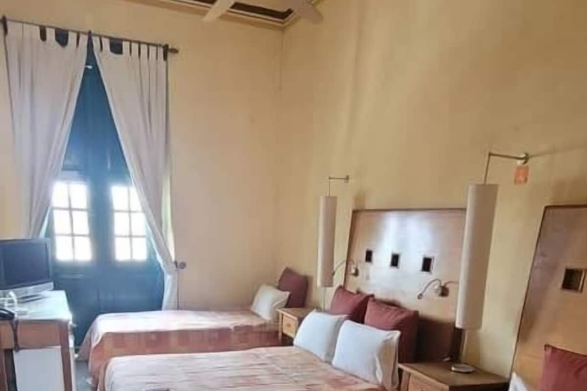A hotel room with three beds, a ceiling fan, a TV, and a window with curtains.
