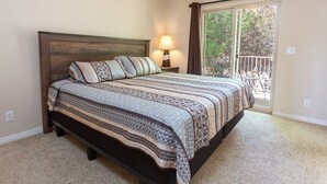 A bedroom with a large bed, a nightstand with a lamp, a window with a view of the outdoors, and a balcony. - Kanab Vacation Rental Condo, Pool, Hot Tub, Gym, 3BR 2BA Close to Zion NP! (Kanab)