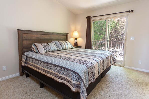 Quarto com uma cama grande, mesa de cabeceira com abajur, janela com vista para o exterior e varanda.