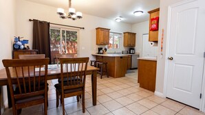 A kitchen with wooden cabinets, a dining table with chairs, a chandelier, and a white door. - Kanab Vacation Rental Condo, Pool, Hot Tub, Gym, 3BR 2BA Close to Zion NP! (Kanab)