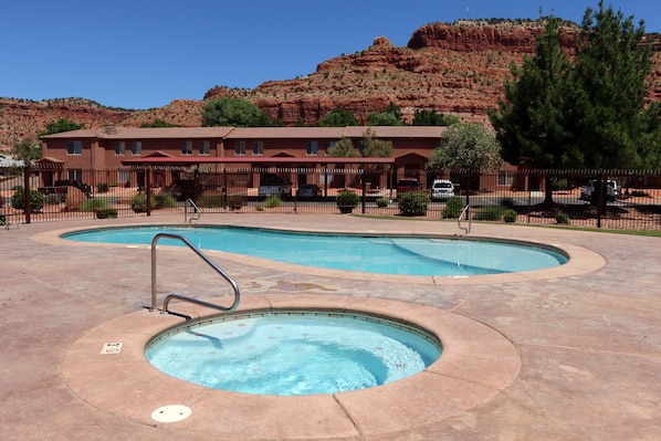 A hotel with a pool area, a mountain backdrop, and a fenced parking lot. - Kanab Red Rock Rental Condo, Pool, Hot Tub, Gym, 3BR 2BA Close to Zion NP! (Kanab)