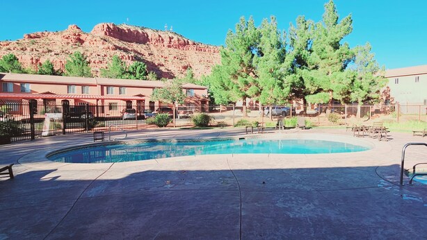A pool area with a circular pool, a wooden deck, and a mountain backdrop. - Kanab Vacation Rental Condo, Pool, Hot Tub, Gym, 3BR 2BA Close to Zion NP! (Kanab)