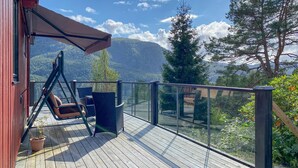 A wooden deck with a swing chair, a glass railing, and a view of mountains.