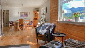 A cozy cabin interior with wooden walls, a dining area, a sofa, and a view of mountains.
